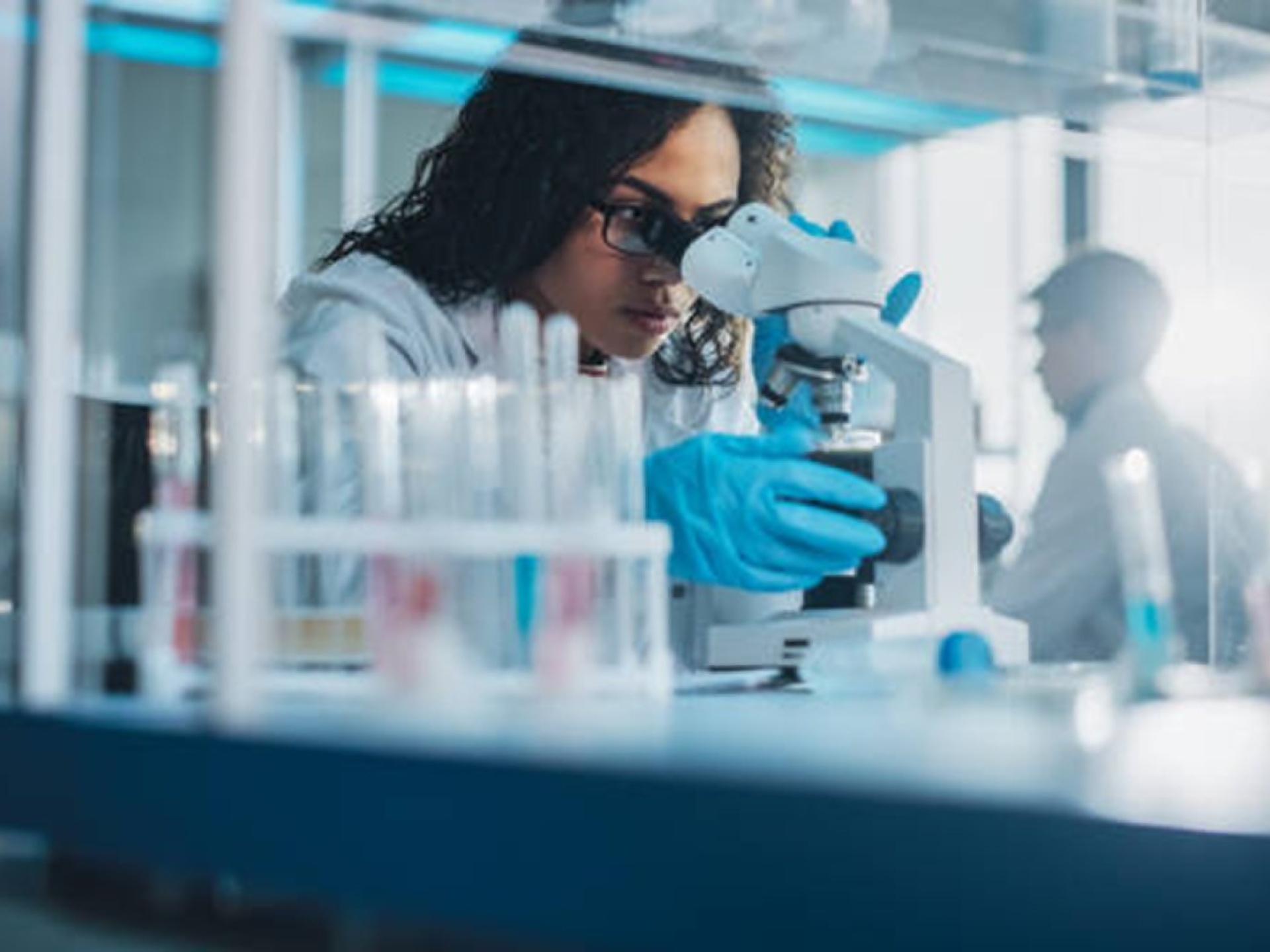 Woman in lab coat reviewing a specimen under a microscope in a lab